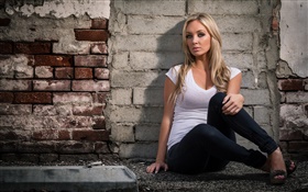 Jeune fille blonde, yeux, est assis à côté du mur